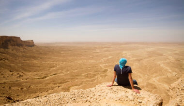 A solo traveler sitting on a cliff in the desert in Saudi Arabia